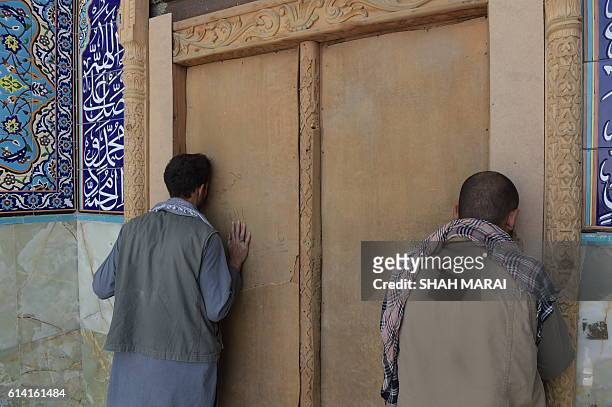 Two Afghan men kiss the door of the Karte Sakhi shrine in Kabul on October 12 after an attack by gunmen late on October 11. Grieving worshippers on...
