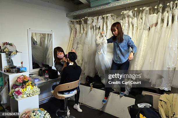 Dress assistant Susan Su takes a wedding dress from a hanger as Echo Li from Shenzhen in China has make-up applied in a studio before changing into a...