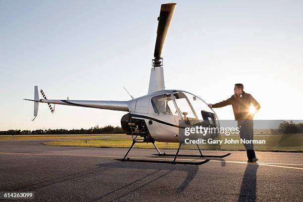 pilot leaning on helicopter at end of day. - helikopter foto e immagini stock