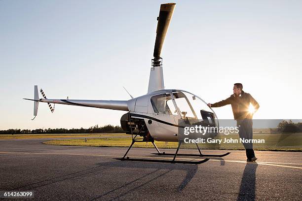 pilot leaning on helicopter at end of day. - helicopter pilot stock pictures, royalty-free photos & images