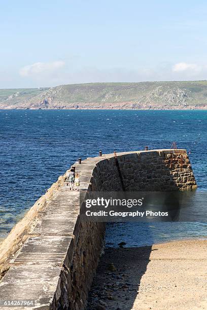 Woman and girl walking on breakwater quay, Sennen Cove, Land's End, Cornwall, England, UK.