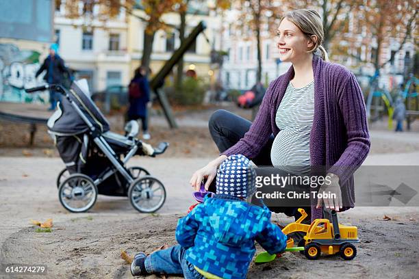 pregnant mom playing with toddler on playground - pregnant lady stock-fotos und bilder