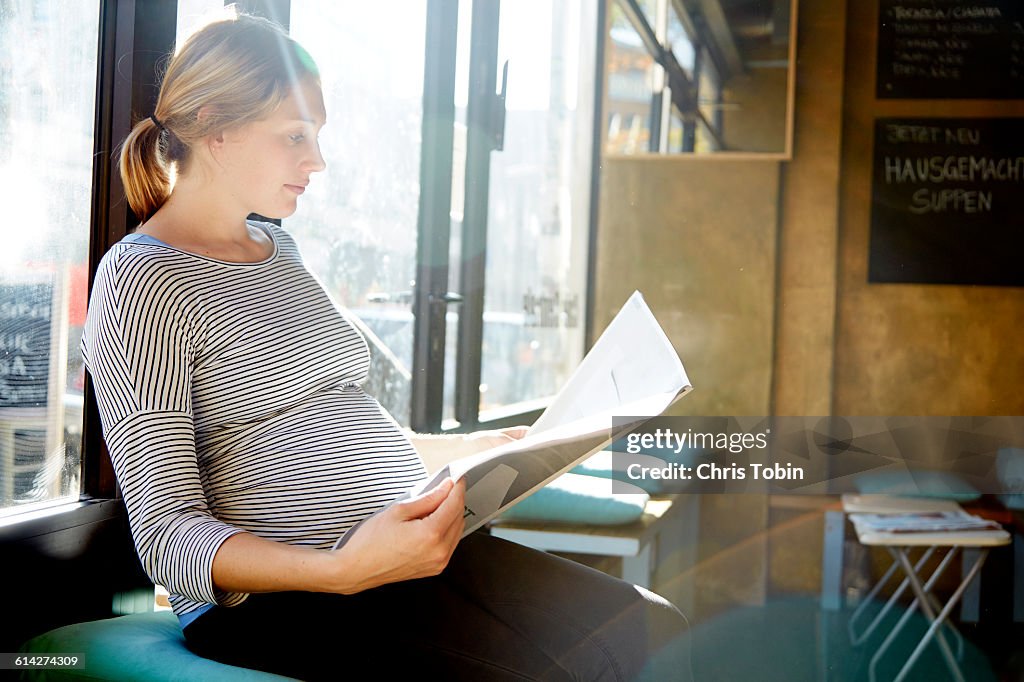 Pregnant woman reading newspaper in café