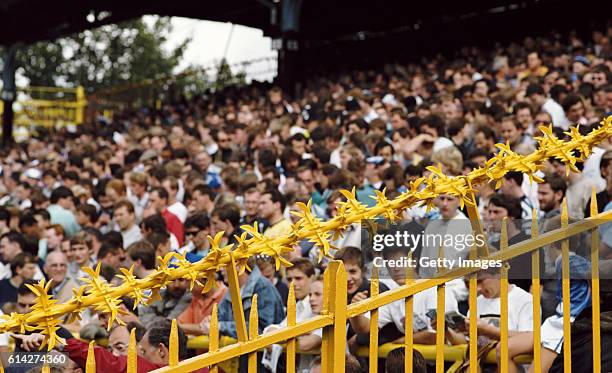 Milwall fans look on from behind A bright yelow spiked 'safety fence' at their Den ground during a match circa 1987, in London, England.