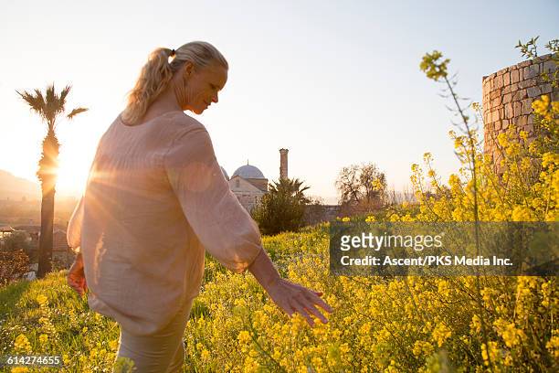 woman strokes flowers while walking through meadow - tuniek stockfoto's en -beelden