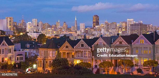 San Francisco California Painted Ladies Victorian homes and city in background at Alamo Square at Hayes Street and Steiner Street at sunset.