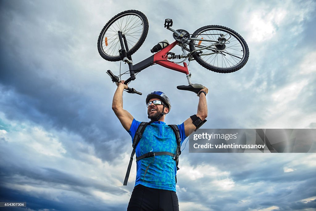Cheerful young man standing on top and lifting his bike