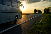 White Bus driving along the asphalt road at sunset.