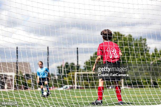 young female kicking a soccer ball towards a male goalie - fat soccer players stock pictures, royalty-free photos & images
