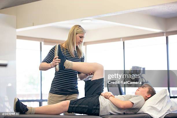 adult female therapist stretching young males leg - postoperatief stockfoto's en -beelden