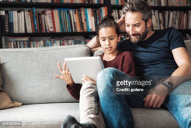 happy father and daughter at sofa looking at digital tablet - teenager learning child to read stockfoto's en -beelden