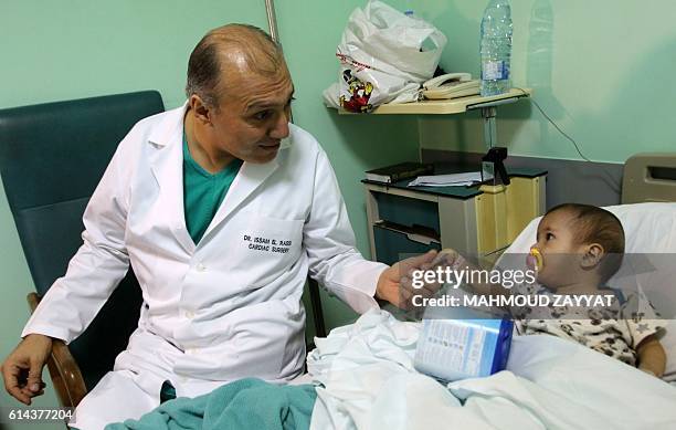 Paediatric heart surgeon Issam al-Rassi holds hands with nine-month-old Syrian refugee Amena al-Helou prior to operating on her heart at the Hammoud...