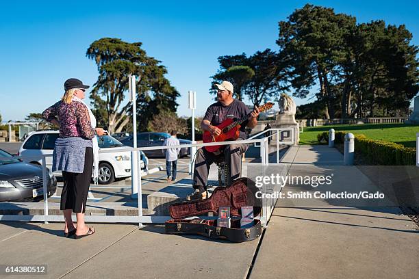 Woman pauses and speaks with a man who plays a guitar while busking in front of the California Palace of the Legion of Honor in the Lands End...