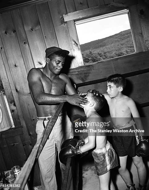 Floyd Patterson takes some time out of training to coach a couple of young boys and apply some vaseline to one of the young boys at his training camp...