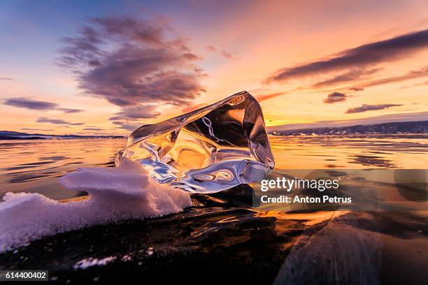 transparent piece of ice at sunset. baikal - eisberg eisgebilde stock-fotos und bilder