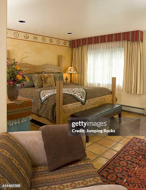 Wood framed bed by window in bedroom with tiled floor, Santa Fe, New Mexico.