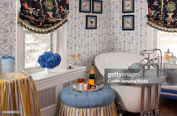 Bathroom with patterned wallpaper and framed pictures above a free standing iron cast bath.