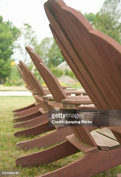Wooden Adirondack sun loungers in a row on grass lawn.