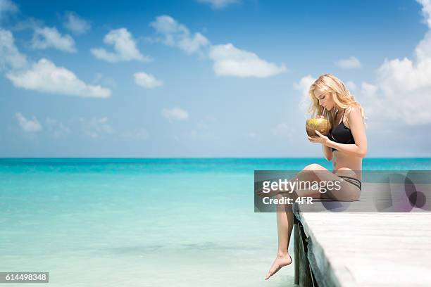 beautiful woman sitting on a pier drinking a fresh coconut - beach model stock pictures, royalty-free photos & images