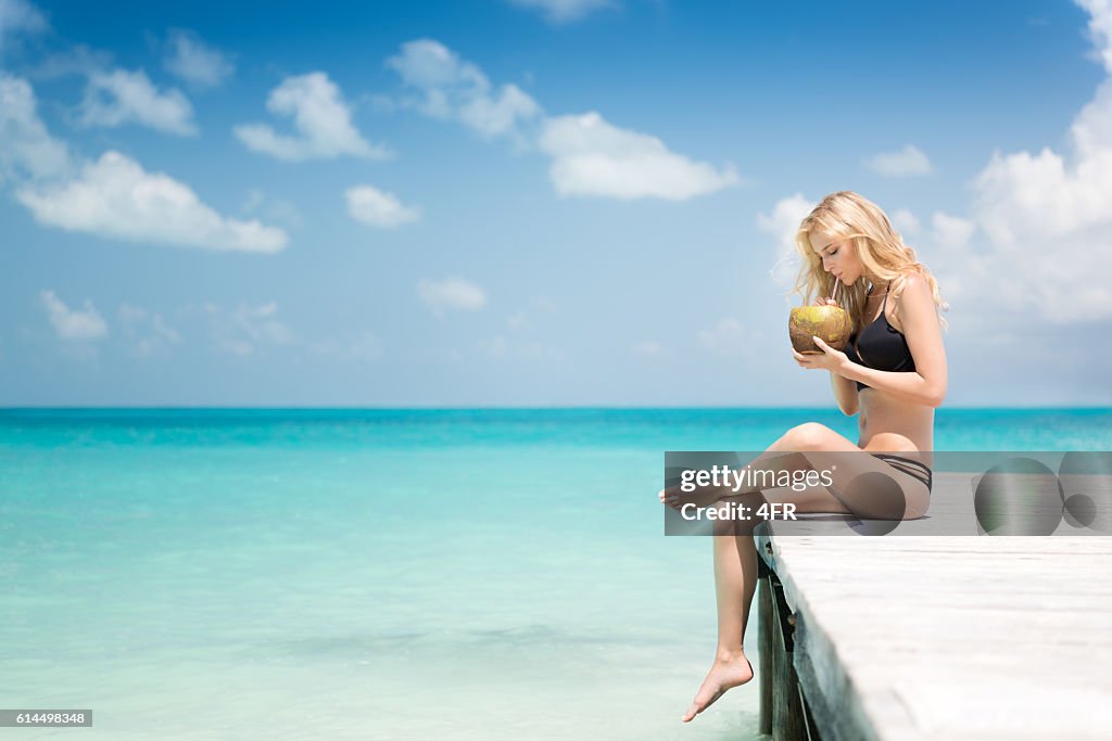 Beautiful woman sitting on a pier drinking a fresh Coconut