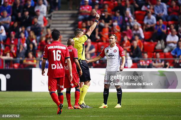 Referee Shaun Evans shows a yellow card to Brendon Santalab of the Wanderers after he made a hard tackle on James Holland of Adelaide United during...