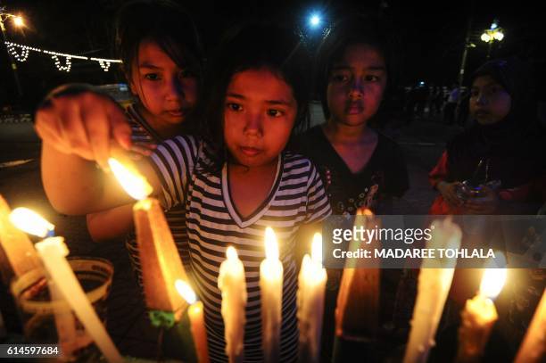 Girls light candles to pay respects to the late Thai King Bhumibol Adulyadej in the southern province of Narathiwat on October 14, 2016. - Massive...