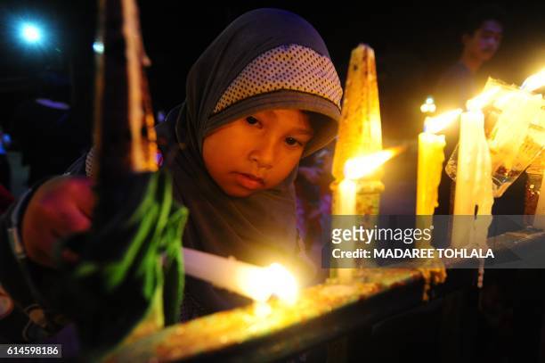 Girl lights candles to pay respects to the late Thai King Bhumibol Adulyadej in the southern province of Narathiwat on October 14, 2016. - Massive...