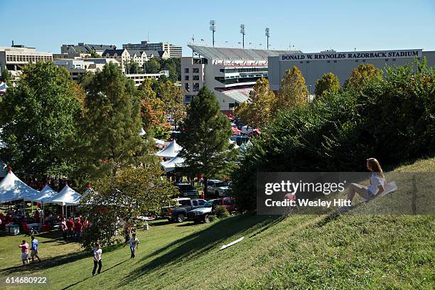 Kids slide down a grassy hill in view of the stadium before a game between the Arkansas Razorbacks and the Alabama Crimson Tide at Razorback Stadium...