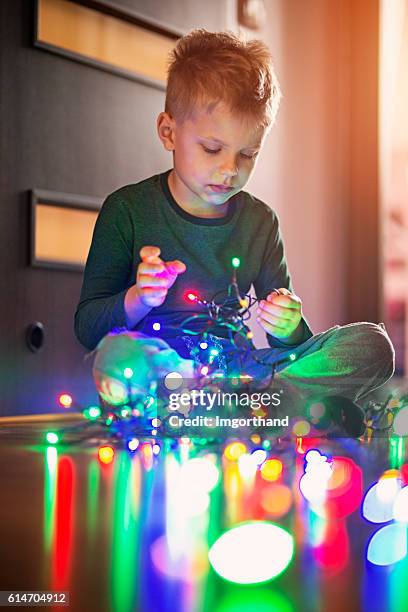 kleiner junge entwirrt weihnachtsbeleuchtung - untangle stock-fotos und bilder