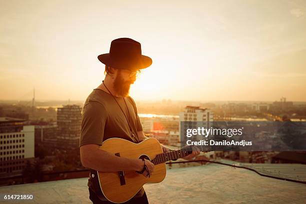 bearded musician playing the guitar on the roof - plectro imagens e fotografias de stock