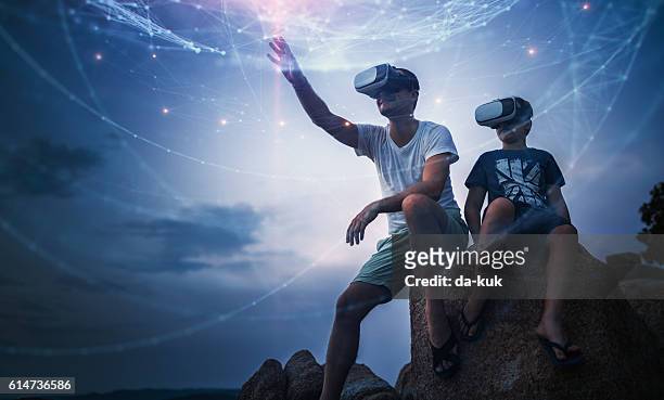 father and son using virtual reality glasses sitting outside - wetenschap en techniek stockfoto's en -beelden