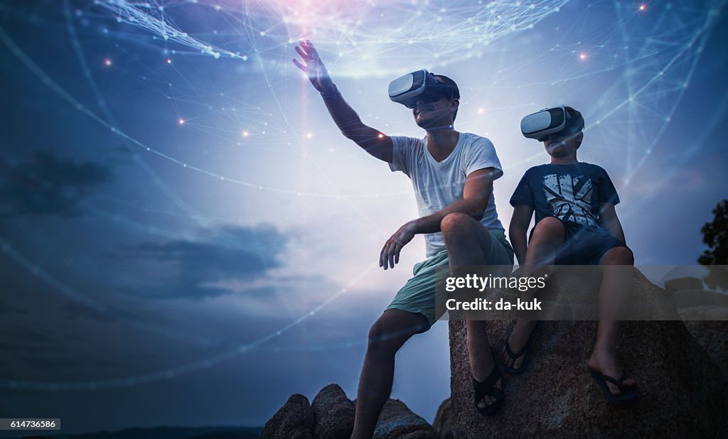 Father and son using Virtual Reality glasses sitting outside