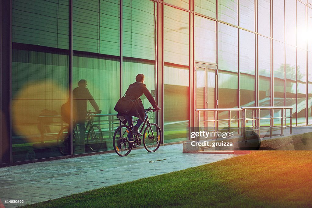 Hübscher Mann mit dem Fahrrad neben dem modernen Bürogebäude