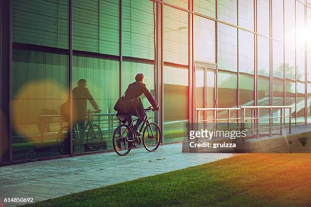 handsome man riding bicycle beside the modern office building - sustainable resources stockfoto's en -beelden
