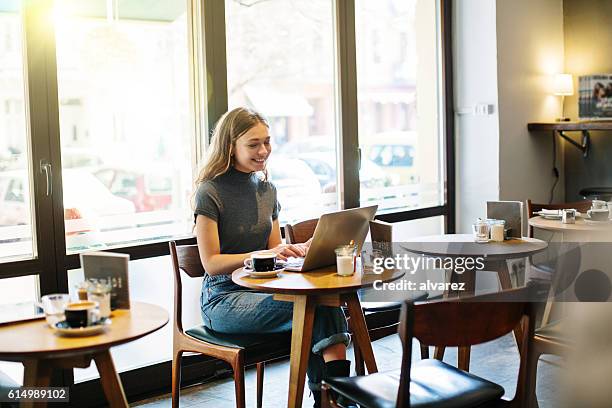 happy young woman at a cafe using laptop - german girl alone stock pictures, royalty-free photos & images