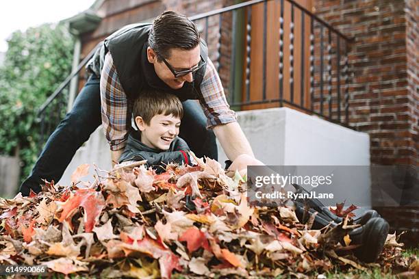 vater und sohn spielen in herbstblättern - rechen stock-fotos und bilder