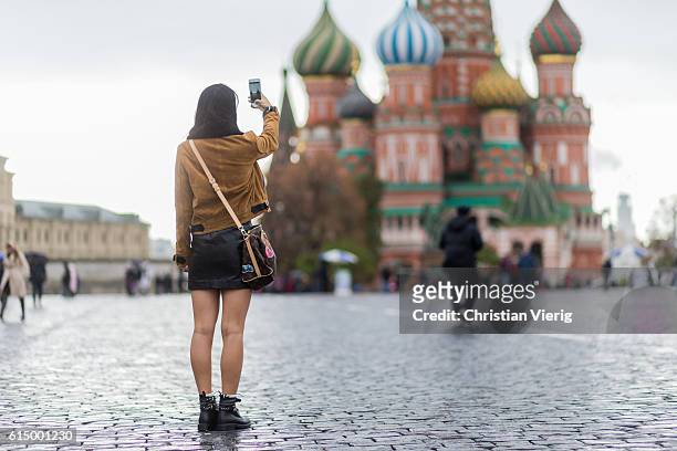 Yuwei Zhangzou taking tourist photos in front of Saint Basils Cathedral wearing a Louis Vuitton bag on October 15, 2016 in Moscow, Russia.