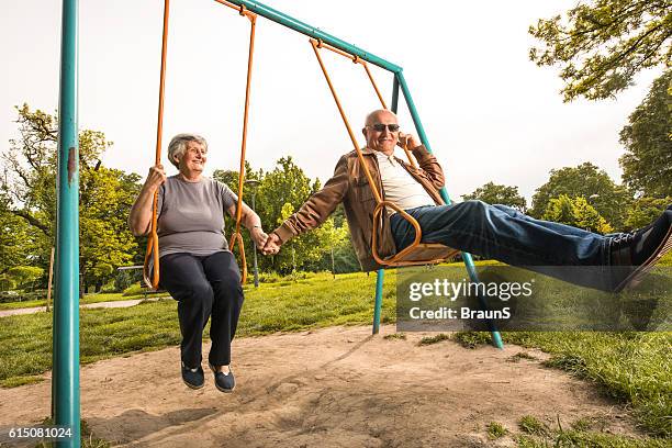 lächelnd seniorenpaar schwingen sich auf den spielplatz. - schaukel stock-fotos und bilder