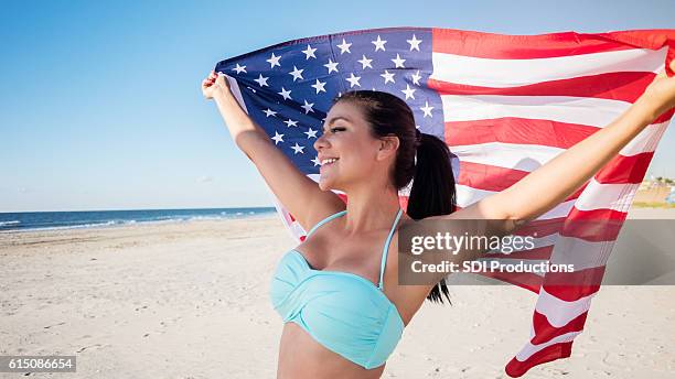 patriotic woman with american flag on the beach - american flag ocean stock pictures, royalty-free photos & images