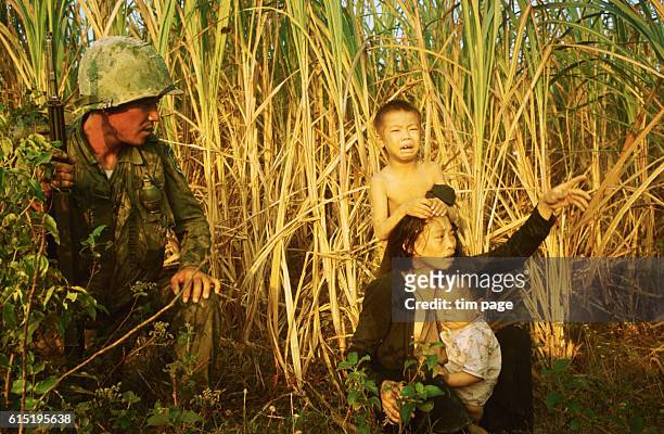 Soldier from the Korean White Horse Division, on an offensive north of Bong Son, kneels beside the bedraggled mother and children of a suspected...