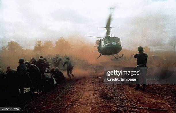 Helicopter takes off from a clearing near Du Co SF camp, Vietnam. Wounded soldiers crouch down in the dust of the departing helicopter. The military...