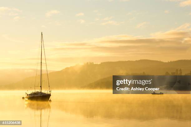 sunrise over men fishing in a boat on lake windermere in ambleside, lake district, uk - ambleside the lake district stock-fotos und bilder