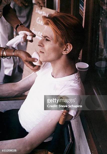 British singer-songwriter and actor David Bowie wearing a white t-shirt as he sits in a chair awaiting makeup in preparation for filming for 'The Man...