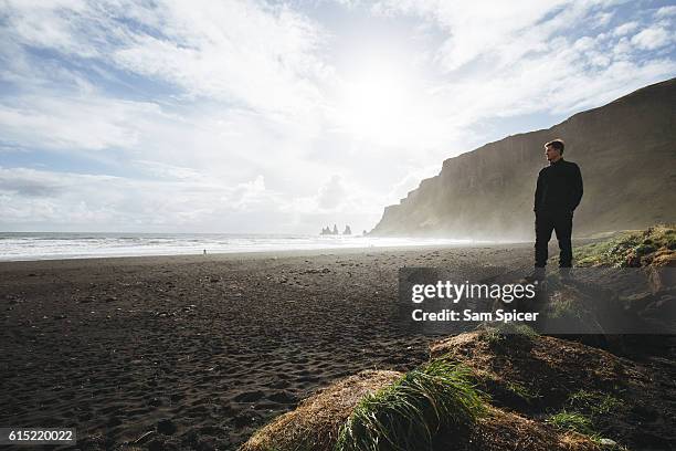 man standing on scenic black sand beach with beautiful sunshine, vik, iceland - black sand stock pictures, royalty-free photos & images