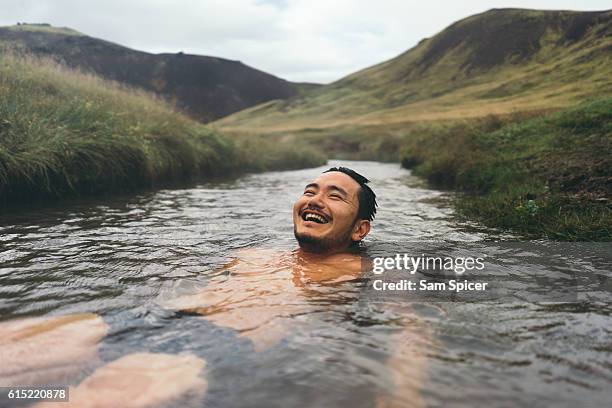 man soaking in natural hot spring surrounded by nature in iceland - warmwaterbron stockfoto's en -beelden