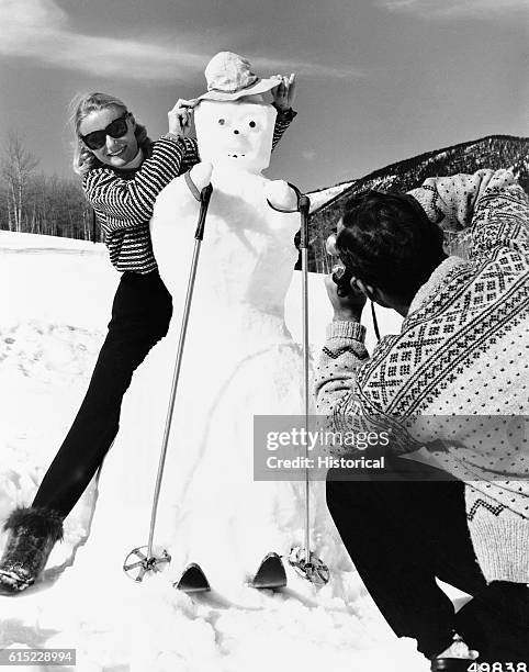 Woman poses with a snowman while a man takes her picture. Aspen, Colorado | Location: Aspen Winter Sports Area, Aspen, White River National Forest,...