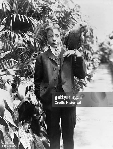 Teddy Roosevelt Jr., son of the president, stands in a garden with a large parrot perched on his hand.