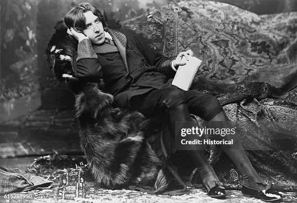 Portrait of poet and novelist, Oscar Wilde, , known for his languid poses and typical costume including a velvet robe and black silk stockings. Wilde...