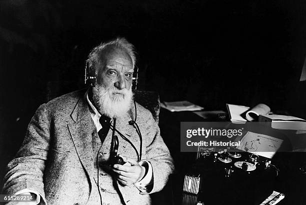 Portrait of Alexander Graham Bell , inventor of the telephone. He wears headphones that are attached to a piece of electrical apparatus.