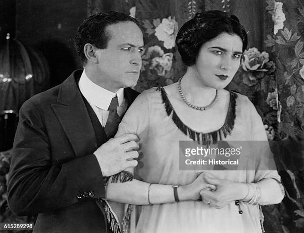 Harry and Beatrice Houdini stand before flowered drapes. Harry Houdini was known for his impressive escape acts.